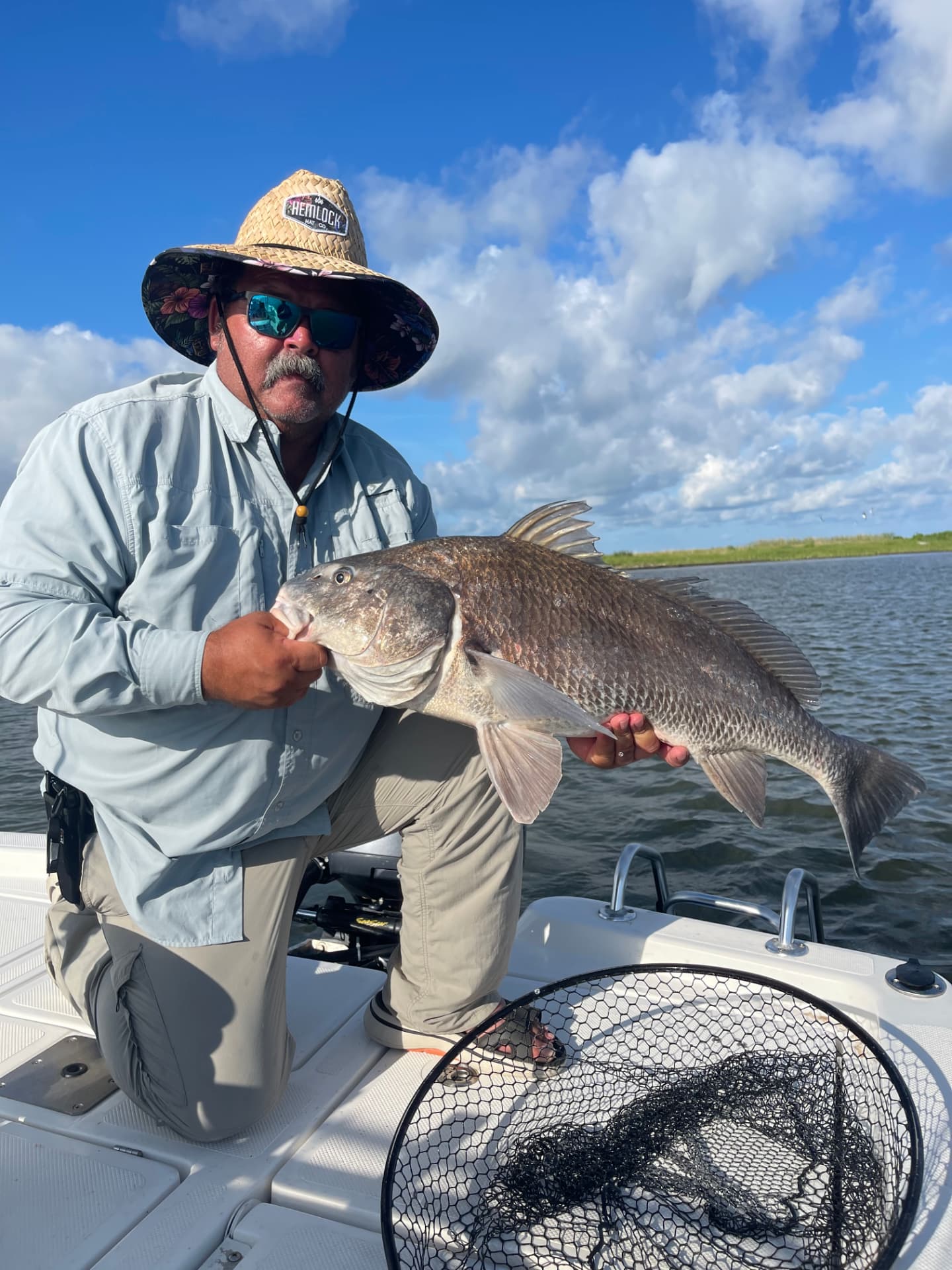 Evan Hightower kneeling on a skiff, holding a large black drum.
