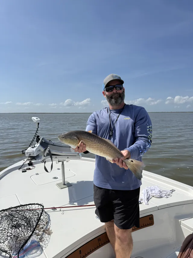 An angler on the bow holds a redfish, a landing net at his feet.