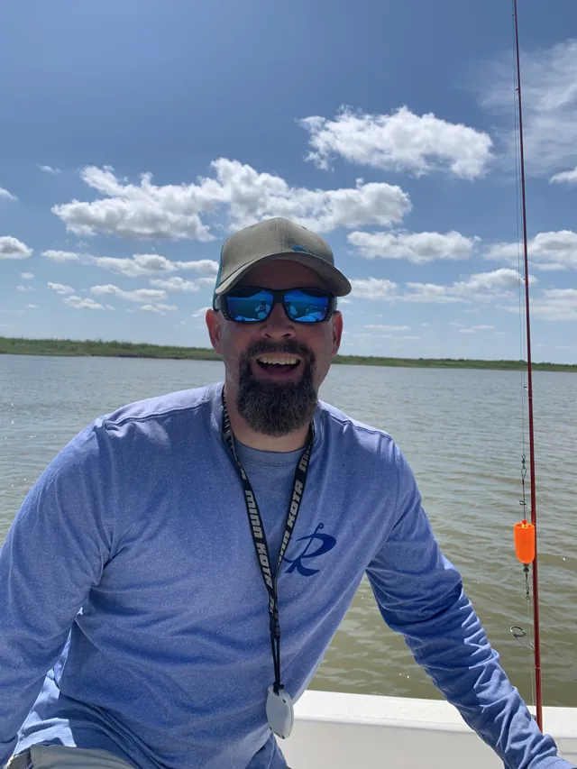 An angler grins at the camera from the boat, a rod bent behind him.