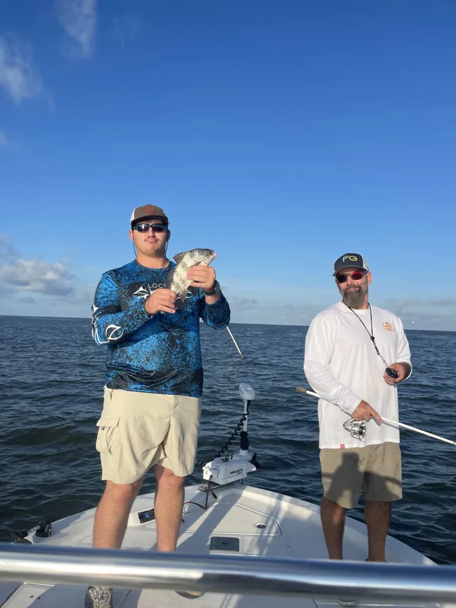 Two anglers on the deck under a clear sky, one holding a fish.