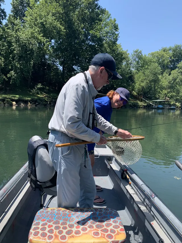 An angler nets a fish over the side of the boat while another leans in to look.